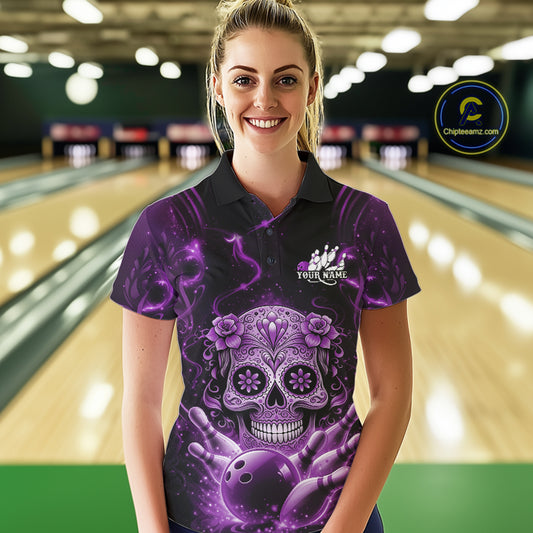 Female model at a bowling lane wearing a black and purple polo shirt with floral sugar skull artwork and bowling-themed graphics.