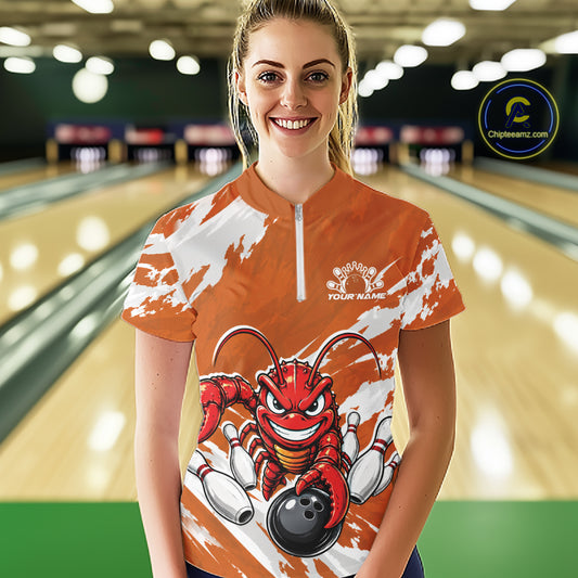 Front view of a happy female model in a bowling alley wearing an orange custom quarter zip bowling shirt with an aggressive crawfish bowling design and a distressed background.