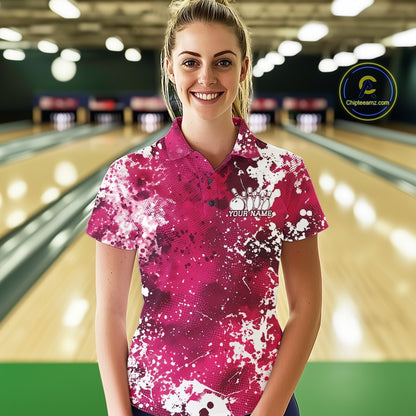 Woman wearing a pink and white patterned bowling shirt with a logo and text in a bowling alley.