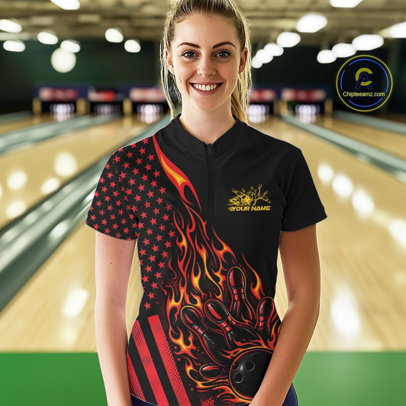 Female model at a bowling lane wearing a black bowling quarter-zip shirt with red-orange flame bowling strike artwork and American flag details.