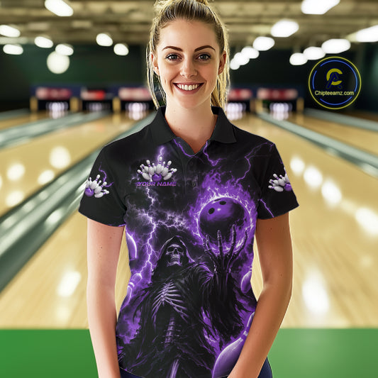 A woman wearing a black short-sleeve polo shirt with a purple and black bowling-themed graphic print, standing in front of a blurred bowling alley background. The shirt features a skeleton, bowling balls, and purple lightning effects.