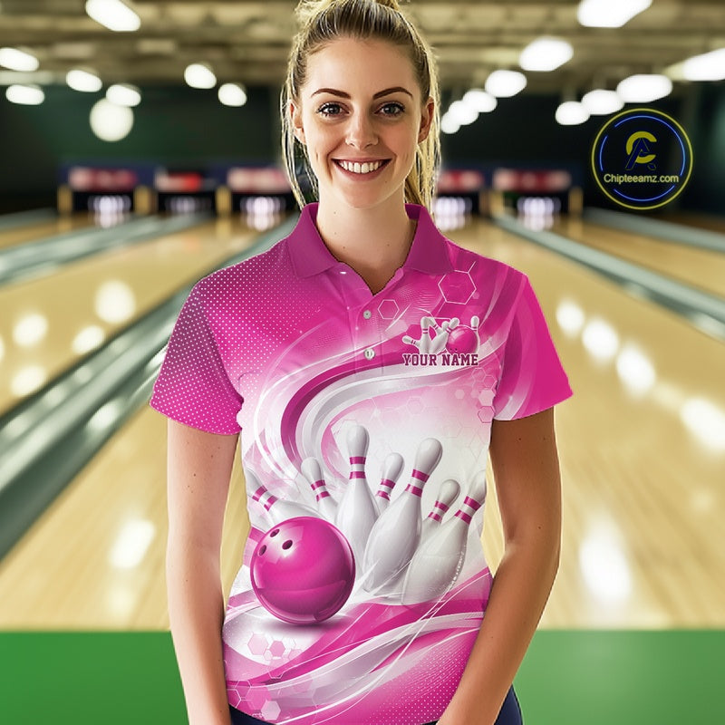 Female model standing in a bowling lane wearing a white and pink bowling polo shirt featuring abstract wave lines and a glossy bowling ball striking pins on the front.