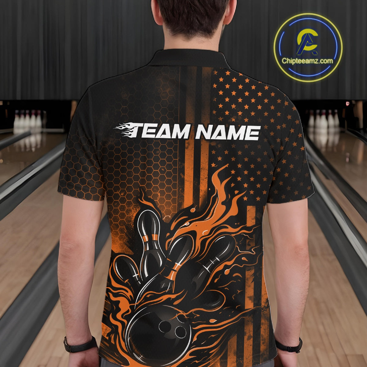 Back view of a male model in a bowling alley wearing a black and orange polo featuring a flaming bowling ball and pins design.
