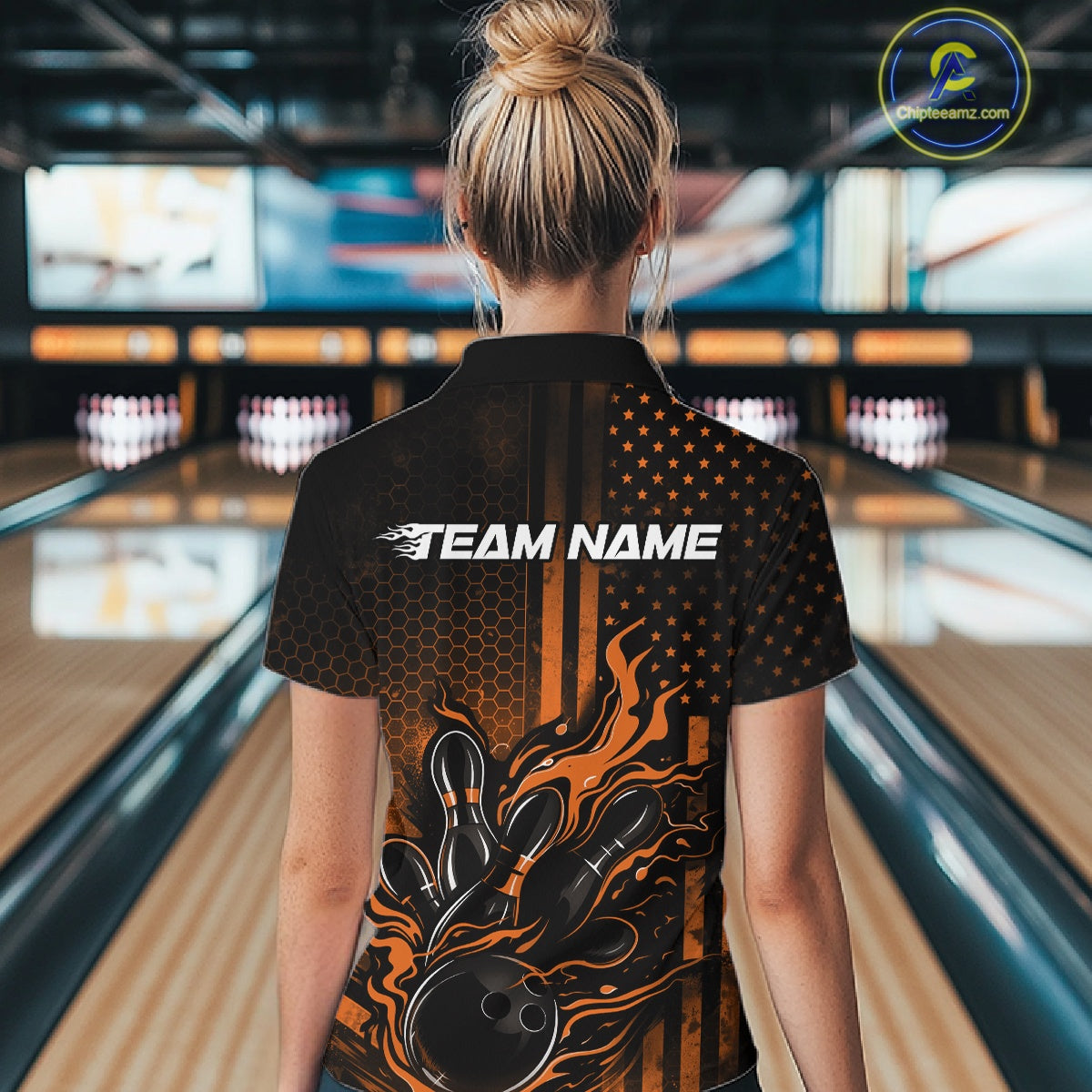 Back view of a female model in a bowling venue wearing a black and orange polo shirt featuring a bowling strike scene with flame accents.