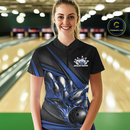 Female model in a bowling lane wearing a black quarter-zip shirt, blue flame bowling ball hitting pins with dynamic stripe-inspired graphics.