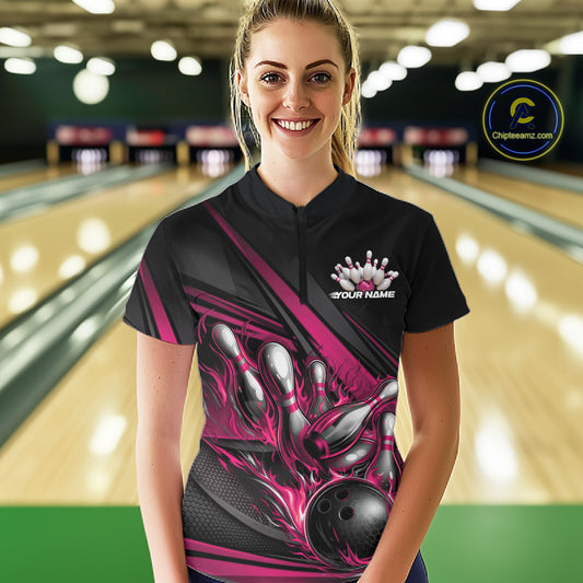 Female model in a bowling lane wearing a black quarter-zip shirt, hot pink flame bowling ball hitting pins with bold geometric stripe styling.