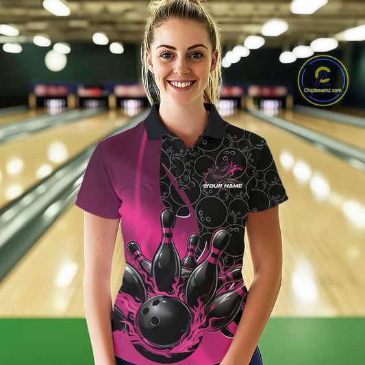 Front view of a female model in a bowling lane wearing a black and pink polo shirt with flaming black bowling ball striking pins and dynamic bowling graphics.