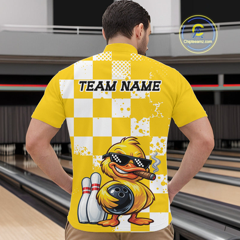 A man viewed from behind wearing a bright yellow bowling-themed short-sleeve shirt with a white checkerboard pattern, distressed splatter details, 'TEAM NAME' printed across the upper back, and a cartoon bowling duck holding bowling pins and a bowling ball. The background shows blurred bowling lanes.