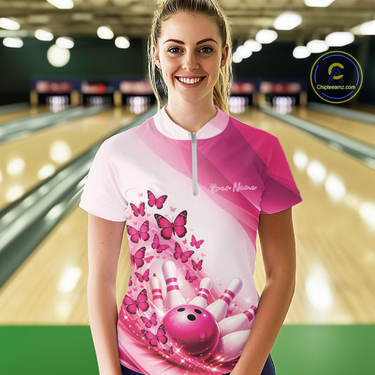 Female model wearing a white and pink bowling quarter zip with butterfly artwork and bowling graphics, front view inside a bowling alley