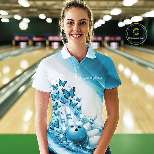 Female model wearing a white and blue bowling polo with butterfly artwork and bowling graphics, front view inside a bowling center