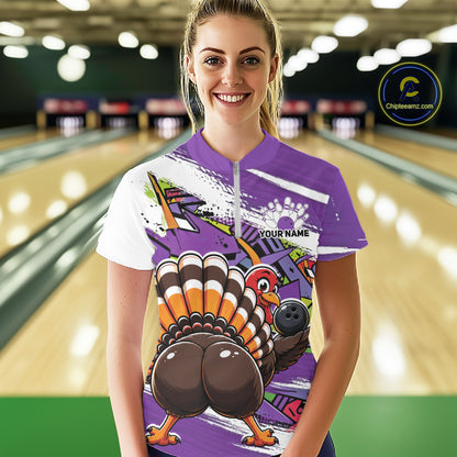 Front view of a happy female model in a bowling alley wearing a purple custom quarter zip bowling shirt with a funny graffiti turkey holding a bowling ball, paint splatter accents, and a personalized name.