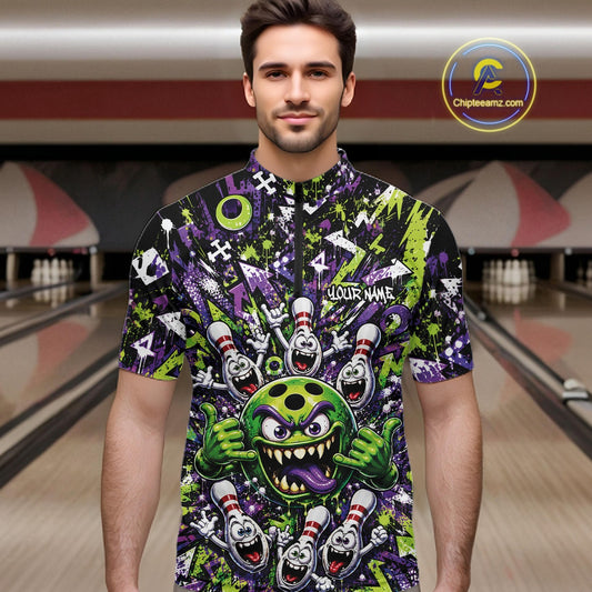 Front view of a male model at a bowling lane wearing a green and purple bowling quarter-zip shirt featuring a mischievous green monster bowling ball with sharp teeth, a purple tongue, playful hand gesture, and cheerful cartoon bowling pins.