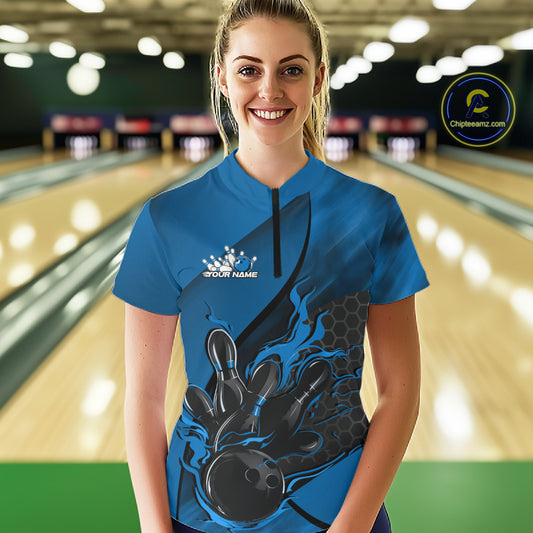 Female model in a bowling lane wearing black and blue quarter zip shirt, front view showcasing flame bowling ball hitting pins dynamic illustration