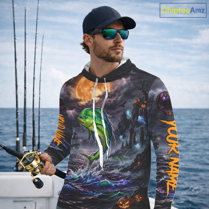 A man wearing a dark hoodie with a detailed all-over graphic print of a green mahi-mahi fish jumping from blue ocean waves under a full moon, holding a fishing rod on a boat. The hoodie features orange text on the sleeves and a white drawstring.