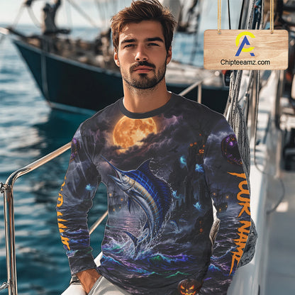 A man wearing a long-sleeve crewneck shirt with an all-over Halloween-themed graphic print featuring a marlin, a full moon, and orange vertical text on the sleeves, photographed on a boat deck with a visible Chipleeamz.com watermark overlay.