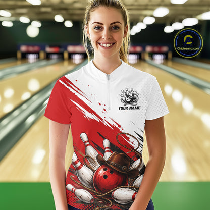 A woman stands in a bowling alley wearing a short-sleeve bowling shirt with a red and white design featuring bowling pins, balls, and a cowboy hat graphic. The right side of the shirt is solid red, while the left side is white with a zipper and a bowling pin graphic.