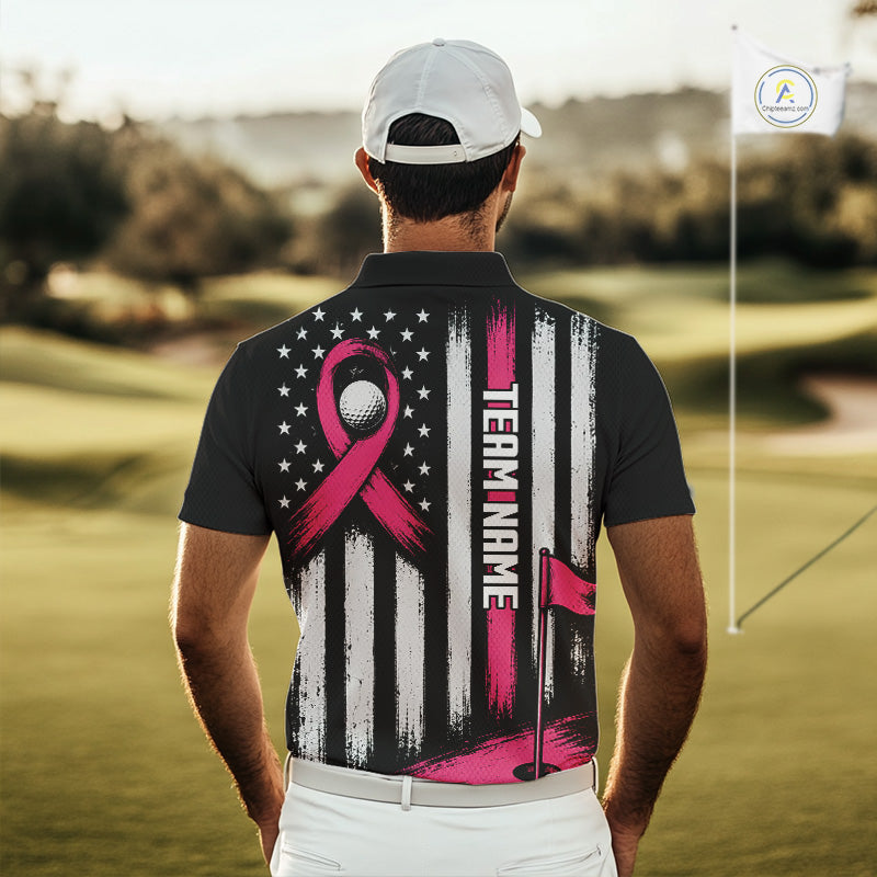 A man viewed from behind on a golf course, wearing a black short-sleeve polo shirt with a large back graphic featuring a pink ribbon, white and black vertical stripes, a golf ball motif, and the text 'TEAM NAME'.