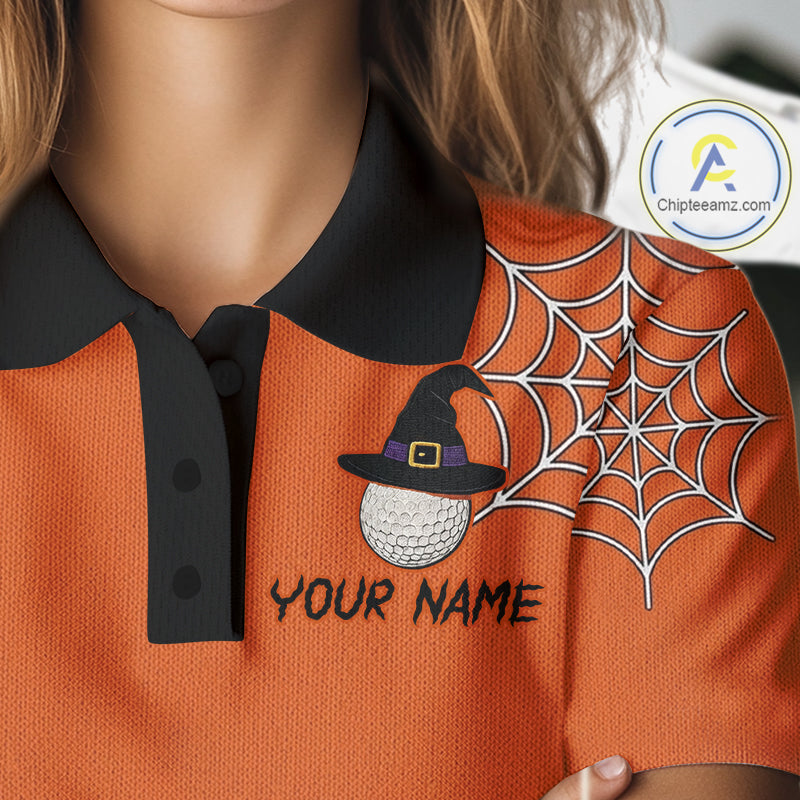 Close-up of a person wearing an orange polo shirt with a black collar. The shirt has a large white spiderweb graphic on the right side, a black witch hat with a gold buckle and purple band over a white golf ball graphic on the left chest, and the text 'YOUR NAME' in black.