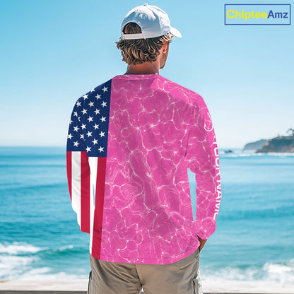 Person wearing a long-sleeve shirt with American flag and pink abstract design by the ocean.