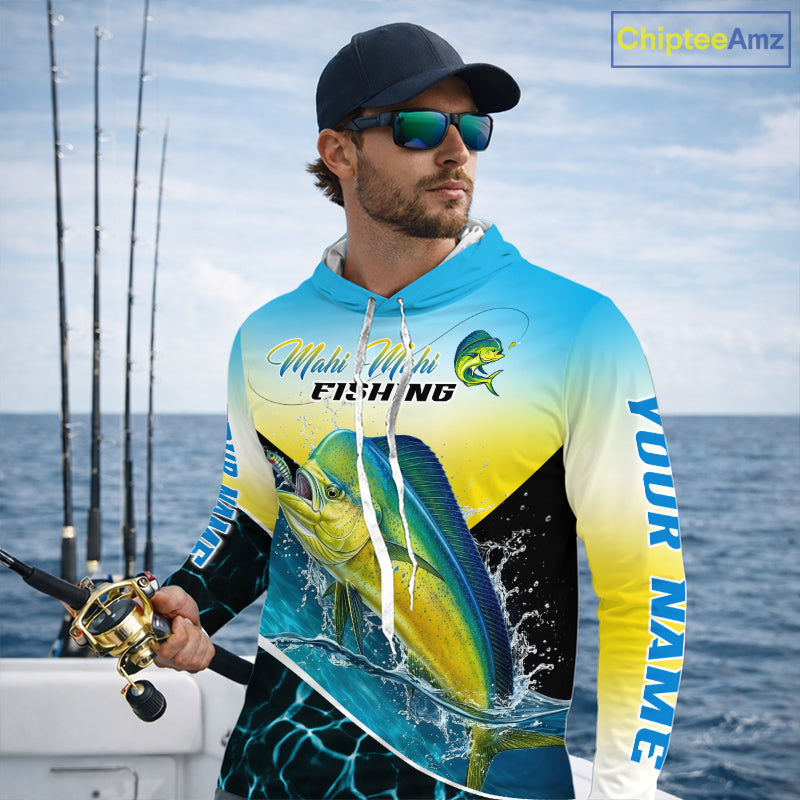 A man wearing a custom blue and yellow gradient fishing hoodie with a large mahi-mahi fish graphic, sunglasses, and a black cap, standing on a boat with fishing rods and the ocean in the background. A 'CustomizeAmz' logo is visible in the top right corner.