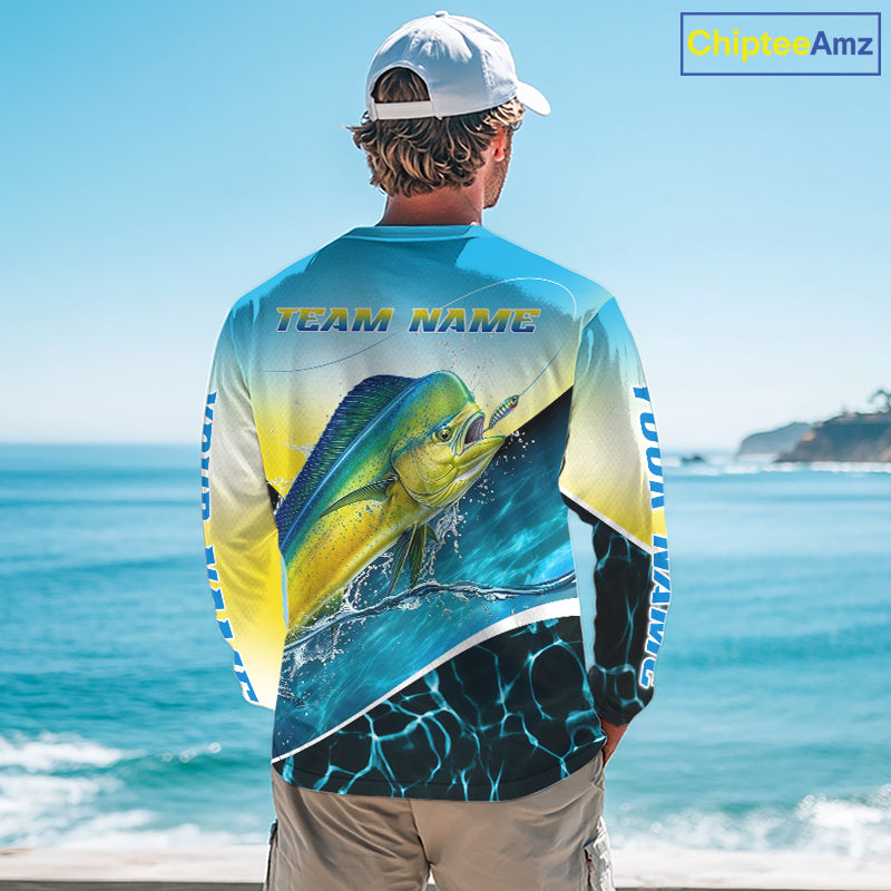 A man viewed from behind wearing a long-sleeve graphic fishing shirt with a large mahi-mahi fish print and 'TEAM NAME' text on the back, standing at a beach with the ocean in the background. A 'ChipteeAmz' logo appears in the top right corner.