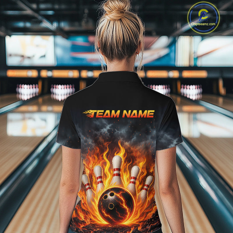 A woman viewed from behind wearing a black short-sleeve bowling shirt with a fiery graphic of a burning bowling ball and pins on the back, standing in a bowling alley.