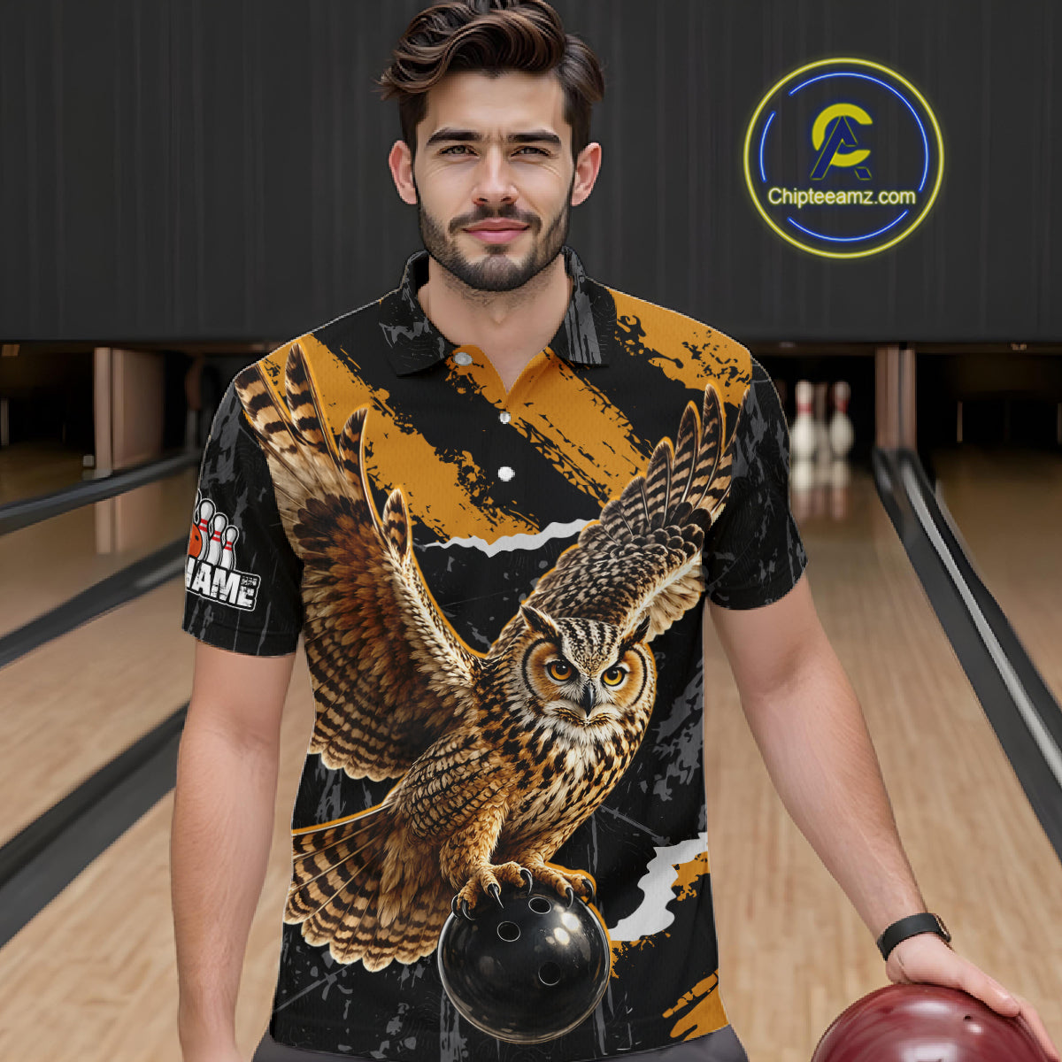 A man in a bowling alley wearing a short-sleeve button-up shirt with a large owl graphic on the front. The shirt has a black and gold pattern with a detailed brown owl and a bowling ball graphic.
