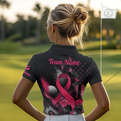 A woman on a golf course seen from behind, wearing a black short-sleeve polo shirt with a pink and gray graphic design featuring a ribbon, golf balls, and the text 'Team Name'.