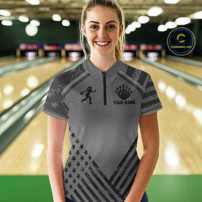 Front view of woman wearing a grey American flag bowling quarter zip shirt inside a bowling alley.