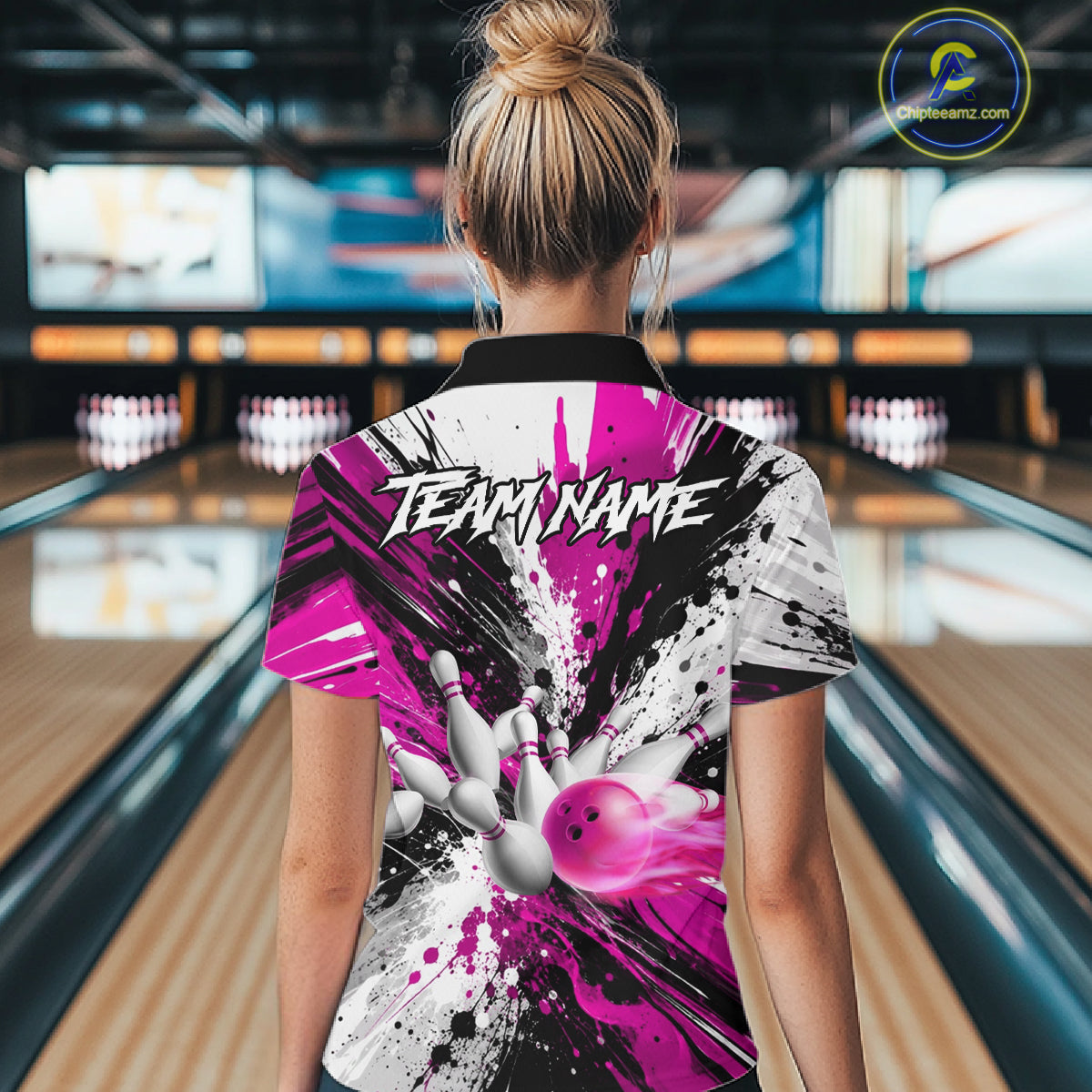 Back view of woman wearing a pink splatter bowling polo shirt inside a bowling alley.