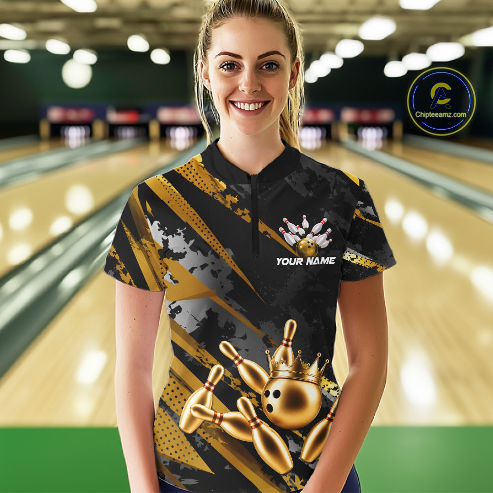 Woman wearing a black and gold bowling shirt with a crown design in a bowling alley.